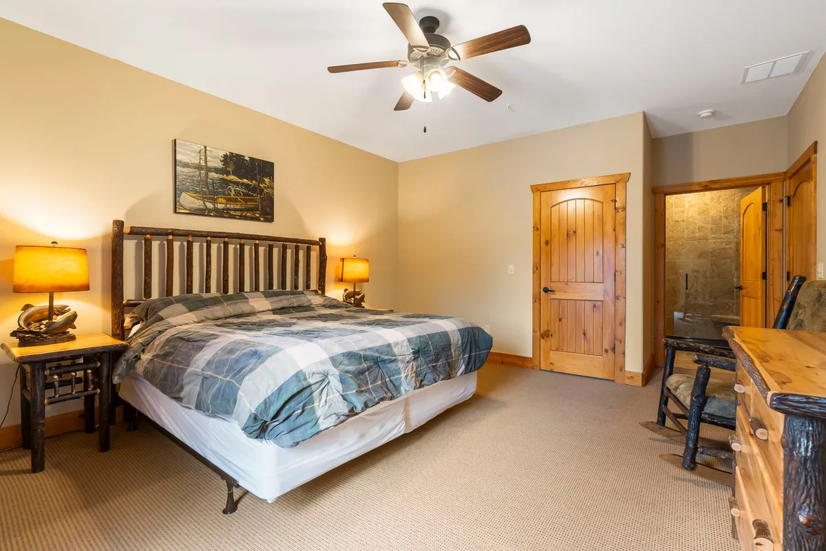 A tranquil bedroom featuring a king-size bed with plush bedding, rustic wooden furniture, and artwork on the wall. Sunlight gently illuminates the room, creating a cozy and restful atmosphere ideal for relaxation.