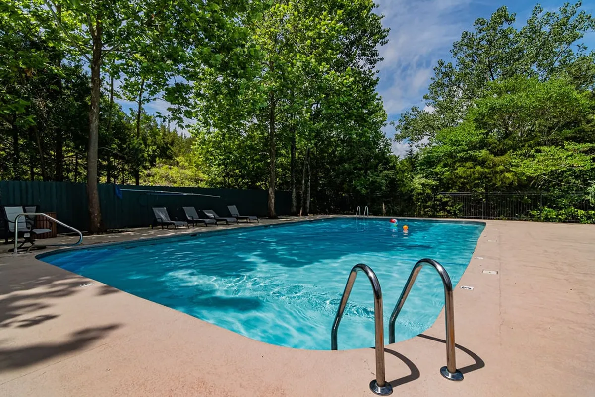 This image features the resort's outdoor swimming pool surrounded by sun loungers and lush trees, evoking a sense of relaxation and recreation. The tranquil setting offers inviting spaces for both swimming and sunbathing, with natural greenery providing a peaceful backdrop.