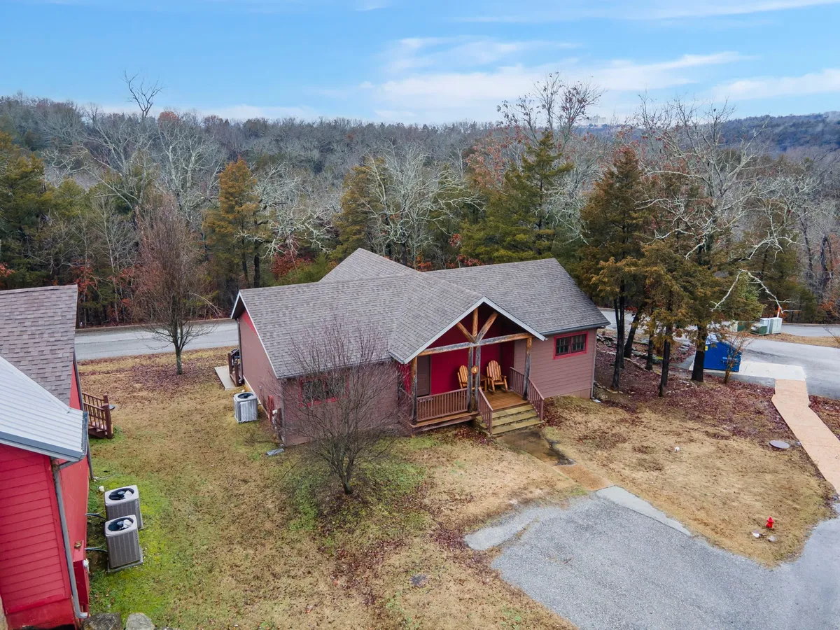 This image showcases a charming red-roofed cabin nestled among trees with a cozy front porch featuring comfortable chairs. The architecture is inviting and surrounded by lush nature, hinting at both privacy and tranquil outdoor enjoyment. The perspective captures the welcoming entry and serene setting, perfect for couples seeking a retreat.