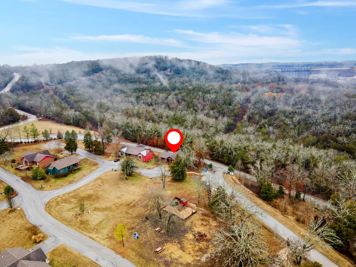 A wide exterior shot showing scenic hills, neighboring resort houses, a playground area, and a winding road. The natural landscape invites outdoor play, hiking, and exploration, illustrating the resort's immersive outdoor environment.