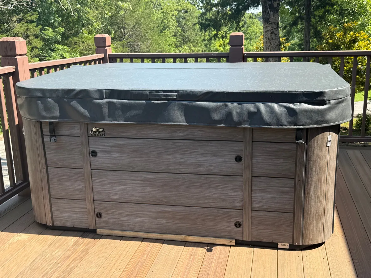 This image showcases a hot tub on the deck with a railing and lush greenery surrounding the space. The scene is set up for relaxation, with the promise of stargazing or morning coffee outdoors.