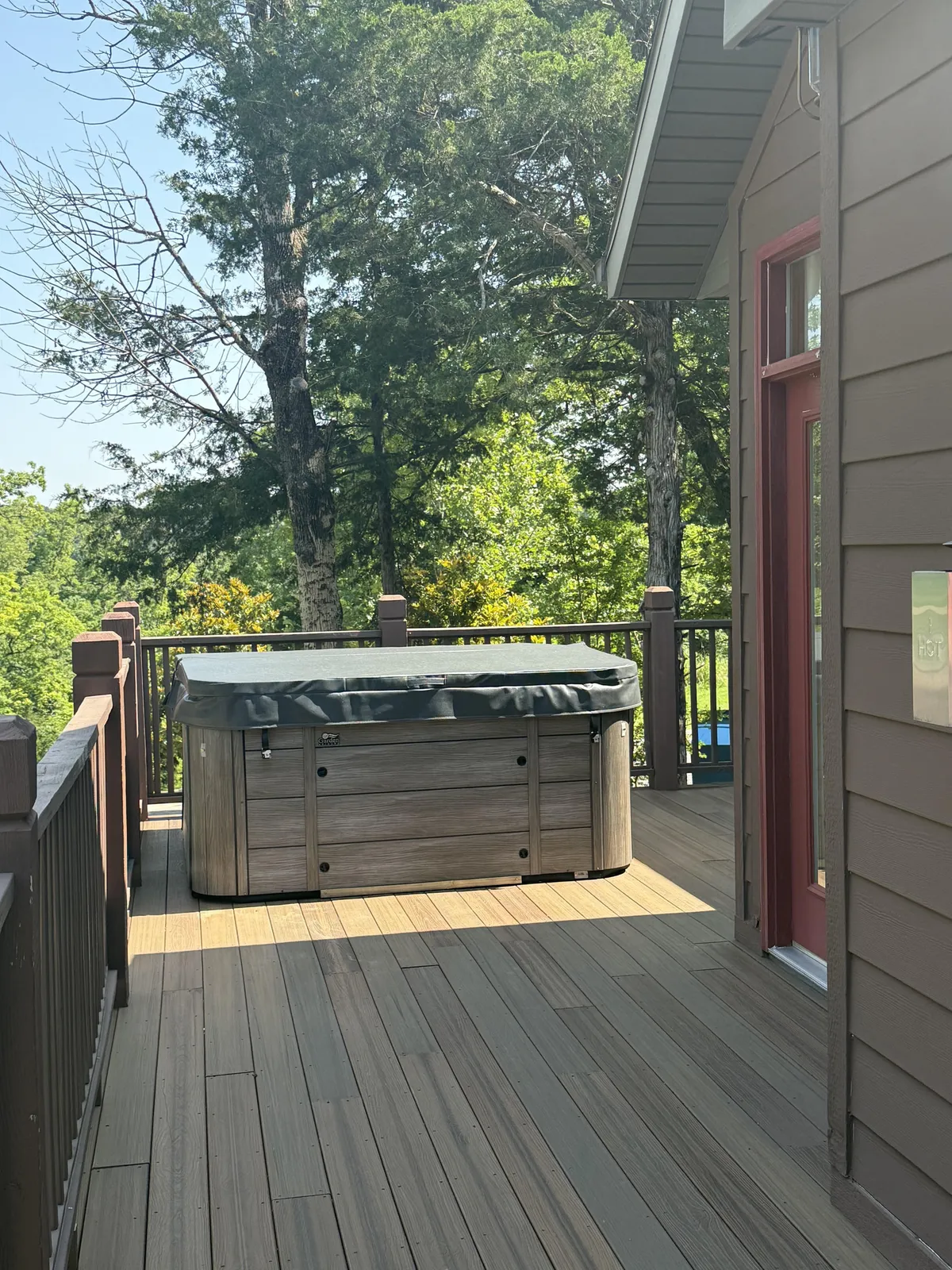 This image features a private deck surrounded by trees, with a hot tub as the focal point. The wooden deck provides ample space for relaxing and socializing, and the setting is tranquil, inviting guests to unwind while soaking in the natural surroundings.