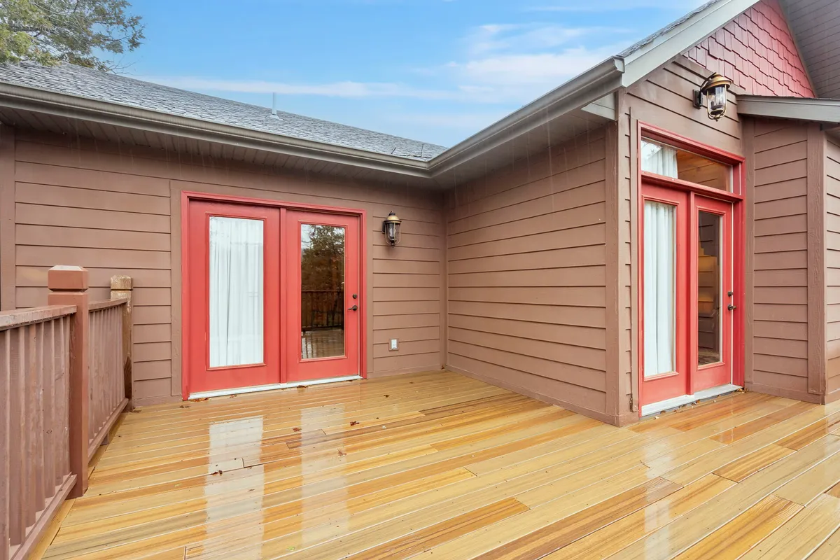 A wide view of the wooden deck featuring bright red doors, with an outdoor light fixture and space for dining or lounging. The deck overlooks natural surroundings, suggesting opportunities for outdoor meals, social gatherings, and enjoying evening relaxation under the stars.