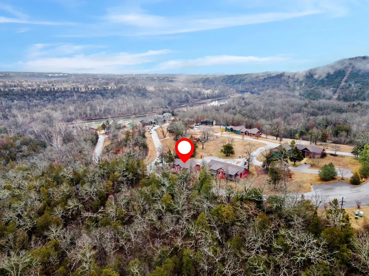 This image captures a scenic view of red-roofed cabins nestled among lush trees, with a winding road leading toward a river visible in the distance. The natural surroundings evoke a sense of tranquility and closeness to the outdoors, ideal for hiking and exploring nearby trails.