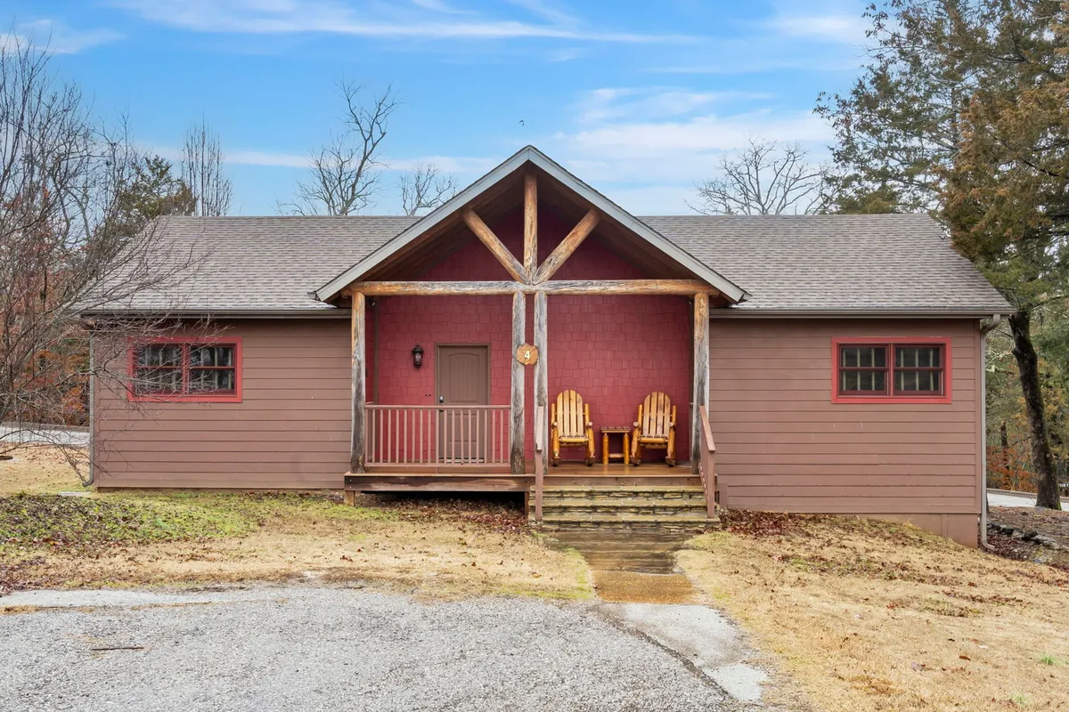 A welcoming front porch with wooden chairs and decorative beams, nestled among trees. The stone pathway and inviting seating invite gatherings, making it ideal for morning coffee, evening cocktails, or sharing stories with friends in a relaxed setting.