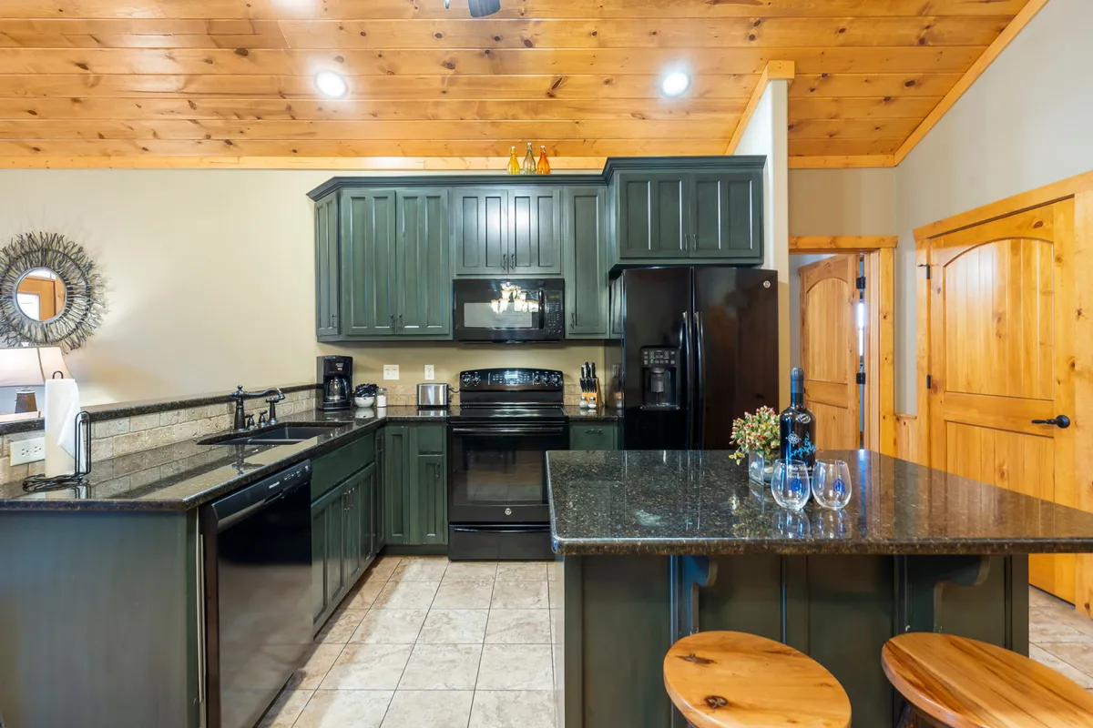 A detailed view of the kitchen area, featuring a granite countertop, dark cabinetry, and a kitchen island beneath a wooden ceiling. The setup is both functional and stylish, suggesting a space well-suited for cooking and gathering.